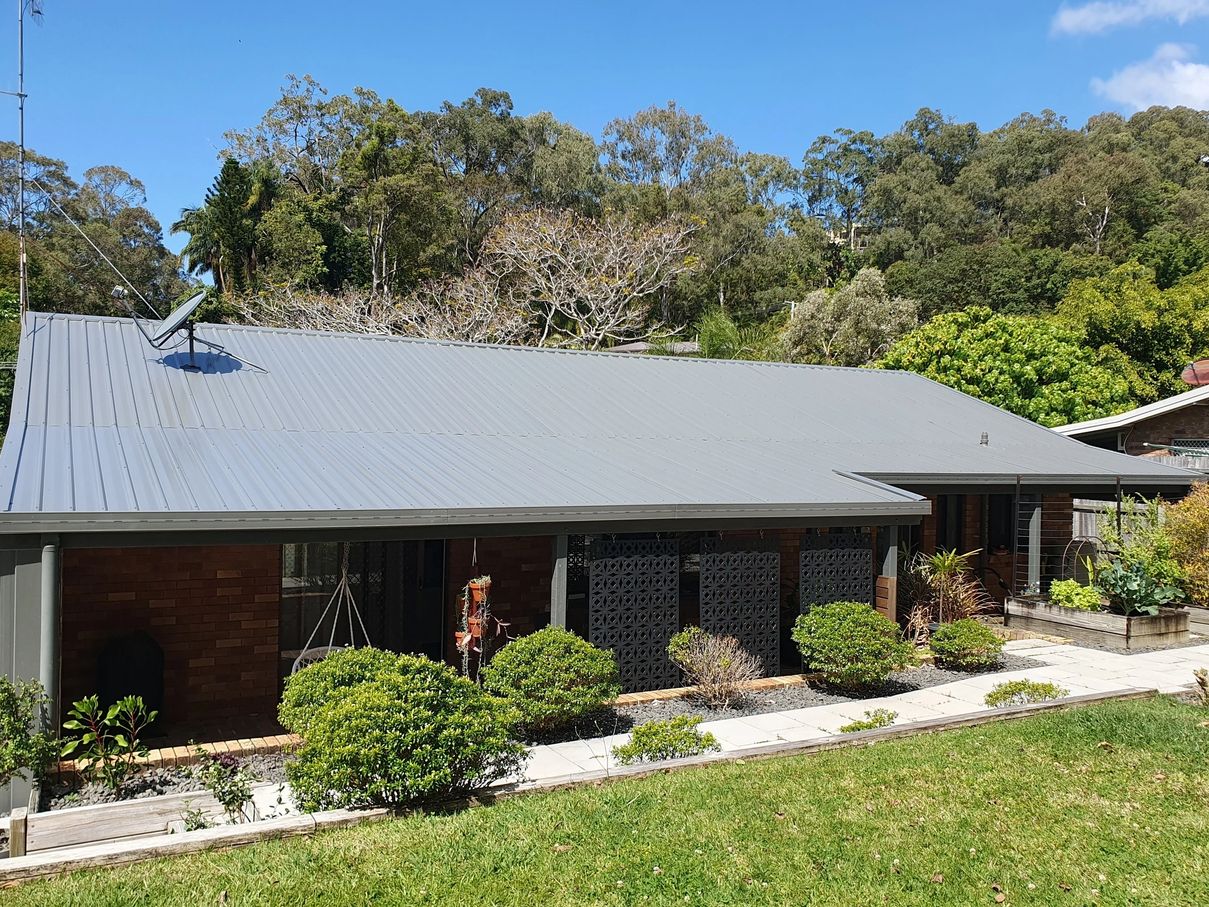 Grey sheet metal roof on a low-set brick home with bushland rising behind it